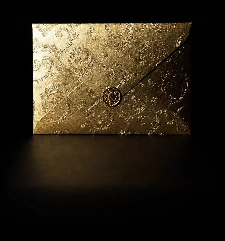 A luxurious gold envelope with subtle embossed floral patterns, sealed with a pointed flap, centred against a deep black background.