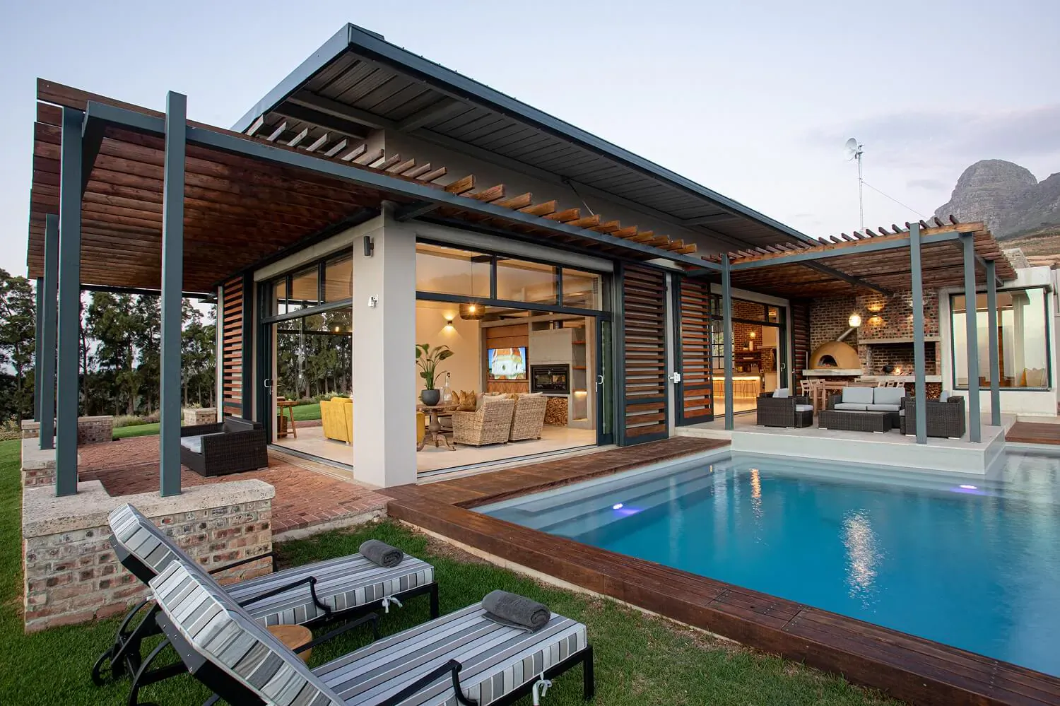 Modern luxury house at Taaibosch Wine Estate with glass walls, infinity pool, lounge chairs, and mountain backdrop