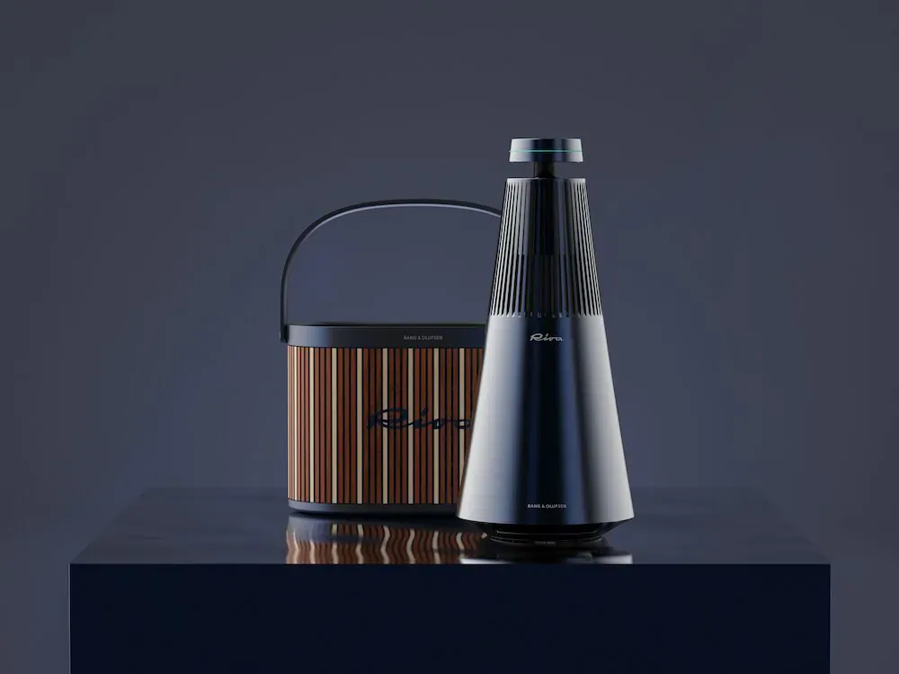 Riva wood-grain portable speaker beside black conical Bang & Olufsen speaker on reflective surface.