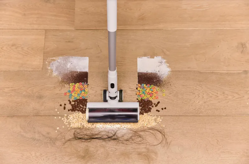 Tineco PURE ONE S15 Pro cordless stick vacuum sucking up cereal, flour, and hair on wooden floor.