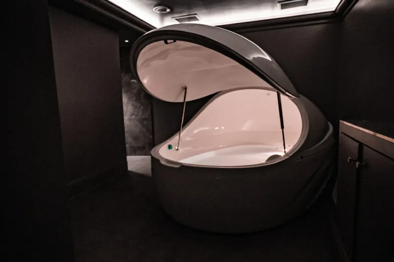 Open futuristic floatation pod with white interior in dark modern wellness room