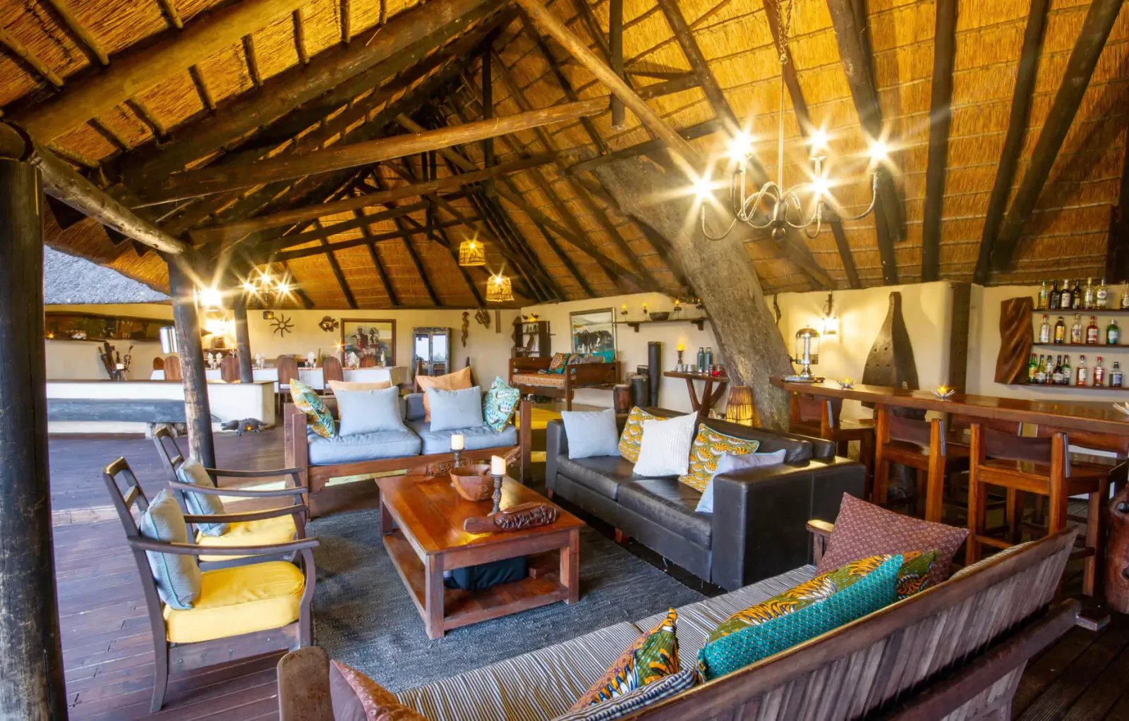 Spacious thatched-roof lodge lounge in Botswana with wooden beams, plush sofas, coffee tables, and bar.