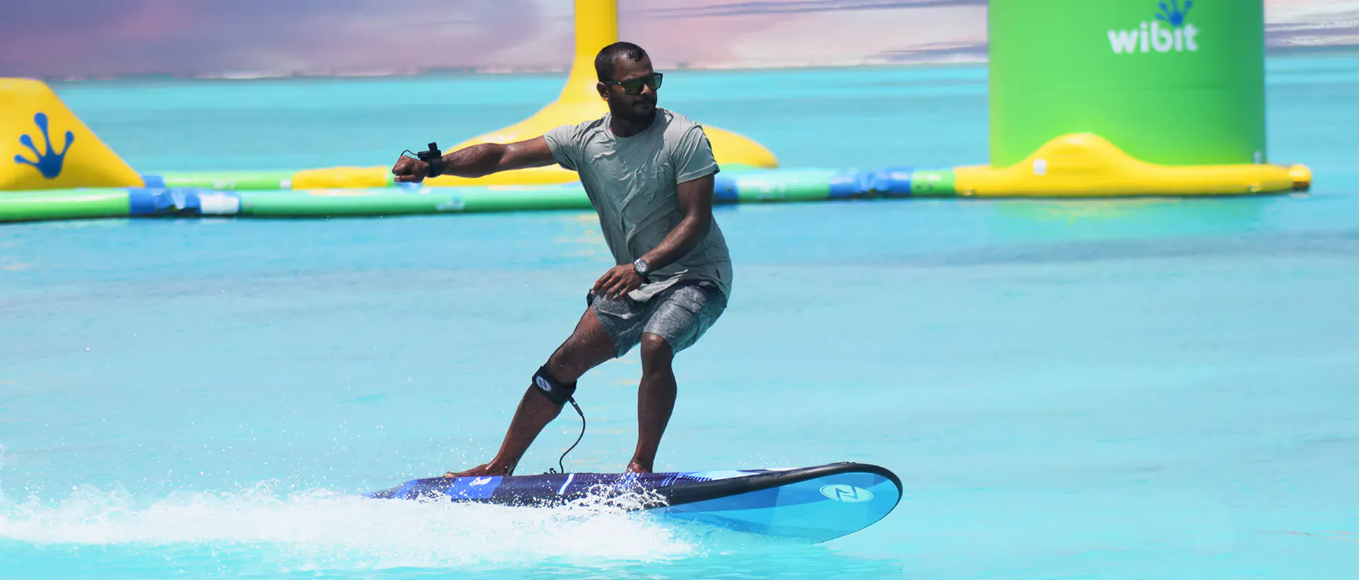 Man riding electric blue surfboard on water obstacle course with Whilt branding and yellow inflatables