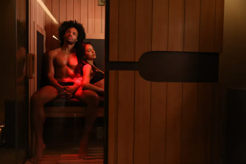 Nude Black couple with red lighting sits intimately on sauna bench at Grey Wolfe London luxury wellness space