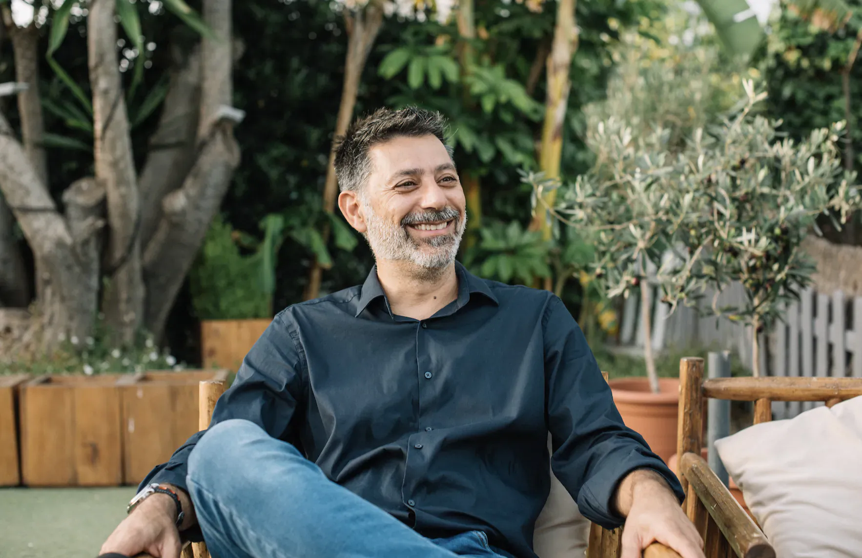 Angelo Collins, founder of Marbella & Beyond, smiling relaxed in wooden chair amid lush garden patio
