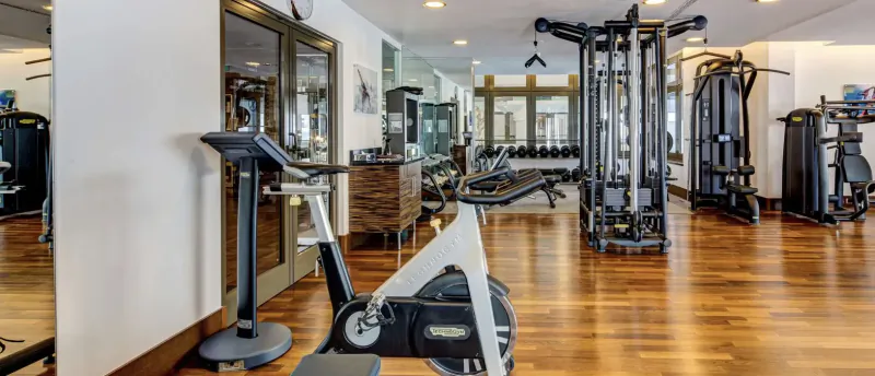 Spacious modern gym at Grand Hotel Des Bains Kempinski St. Moritz with exercise bikes, weight machines, and wood floors