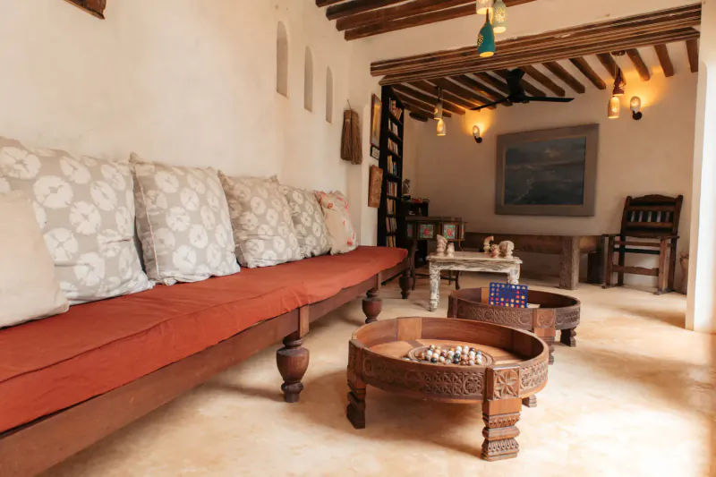 Cozy Swahili room at Kijani Hotel Lamu with red bench sofa, carved wood table set with chessboard, and arched windows.