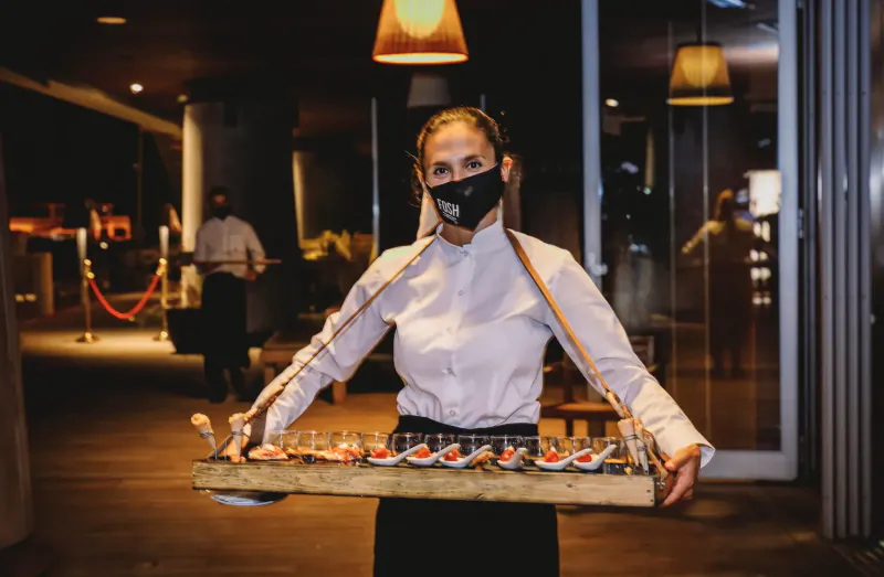 Server woman in black mask and white shirt holding tray of shrimp appetizers at upscale evening event