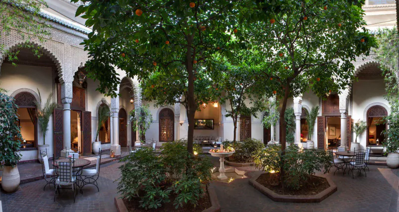 Lush courtyard in Marrakech riad with orange trees, fountain, seating areas, and arched white architecture
