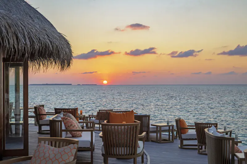 Mirihi Island Resort: Sunset over Indian Ocean with thatched-roof lounge chairs on wooden deck.