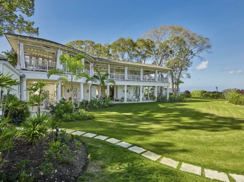 Luxury white multi-level beach house with balconies, surrounded by palm trees and lush green lawn