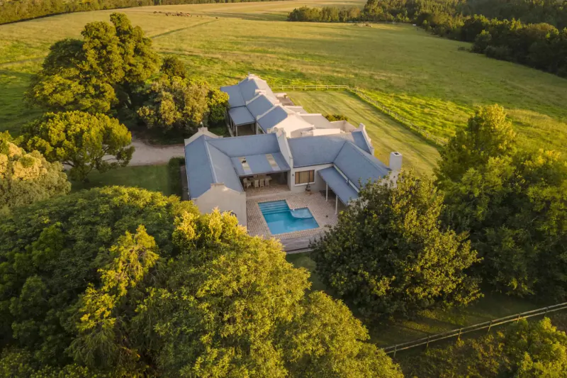 Aerial view of Kay & Monty Vineyards luxury estate with pool, surrounded by green fields and trees on Plett Wine Route