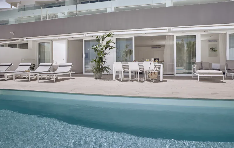 Luxury poolside terrace at Baobab Suites resort in Tenerife with white loungers, dining table, plants, and ocean-view balcony.