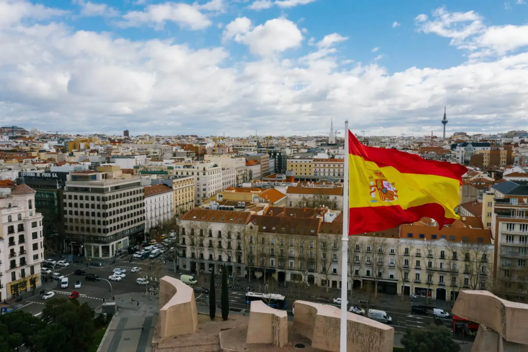 Spanish flag waving over panoramic Madrid skyline with terracotta rooftops and cityscape under blue cloudy sky