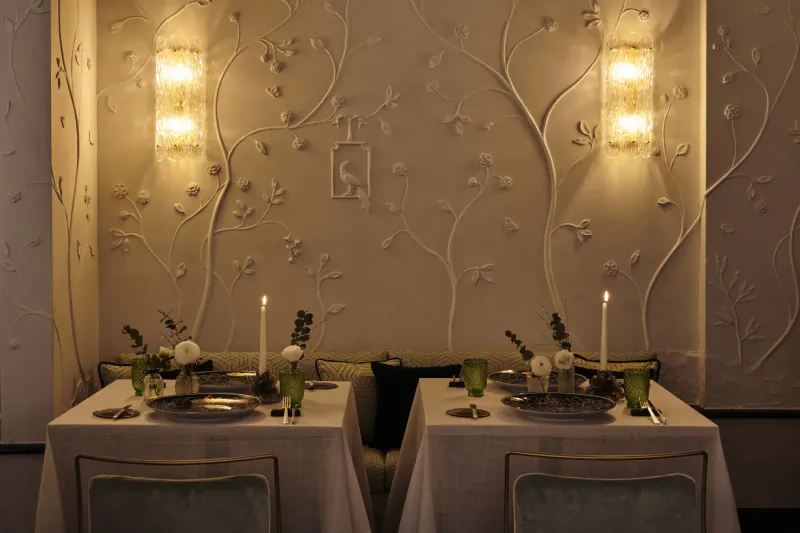 Elegant dining table at Violino d'Oro Hotel Venice, set with white linens, green glassware, candles, and floral decor against ornate wall.