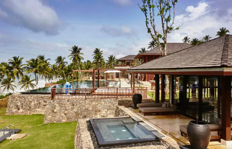 Luxury private resort with infinity pool, hot tub, lounge deck, palm trees, and ocean view under blue skies
