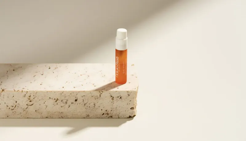 Small amber glass bottle with white dropper on white textured stone surface, soft sunlight shadow, sun protection product