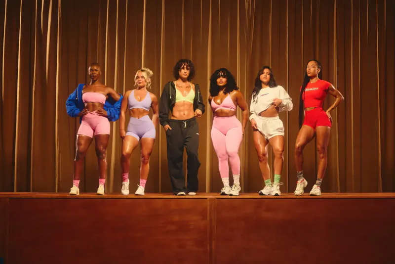 Six diverse women in colorful Oner Active sportswear posing confidently on stage before gold curtains.