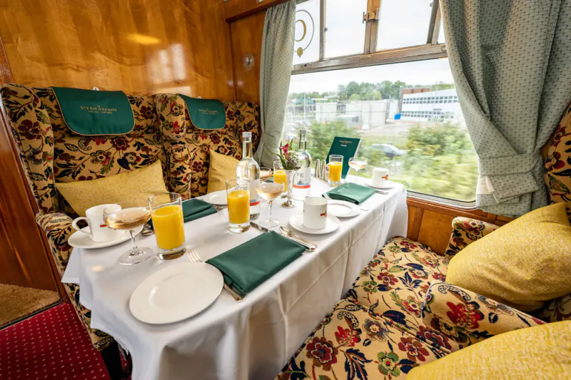 Elegant breakfast table with orange juice, coffee, and pastries in a luxury vintage train dining car with window view.