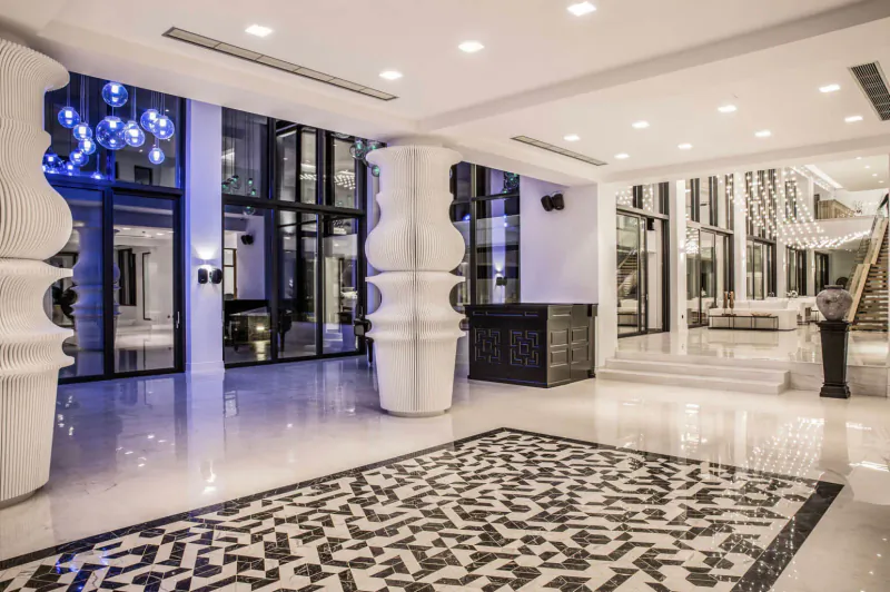 Elegant lobby of Abaton Island Resort & Spa with ornate white columns, blue pendant lights, black-and-white mosaic floor, and large windows.