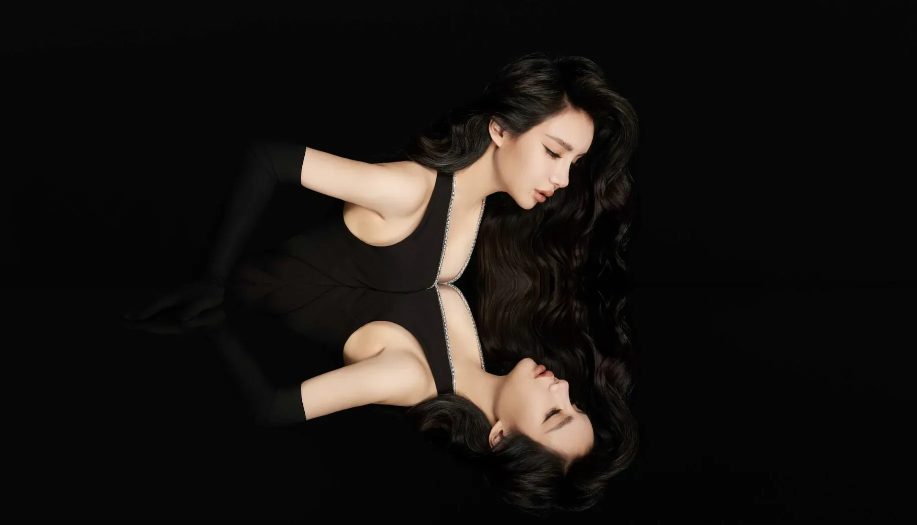 Elegant woman in black sleeveless dress and gloves, mirrored reflection on black background