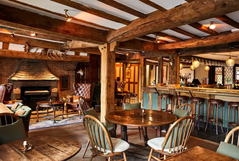 Cozy rustic interior of Hotel Indigo Stratford upon Avon gallery with wooden beams, fireplace, armchairs, and bar.