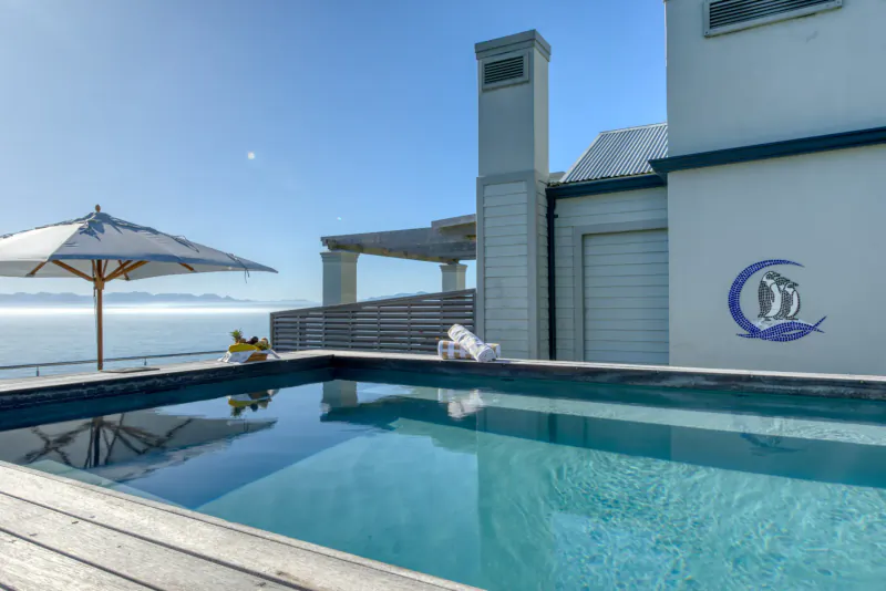 Infinity pool at Tintswalo Boulders luxury coastal retreat, with white umbrellas, lounge chair, ocean view, and crescent moon logo on wall