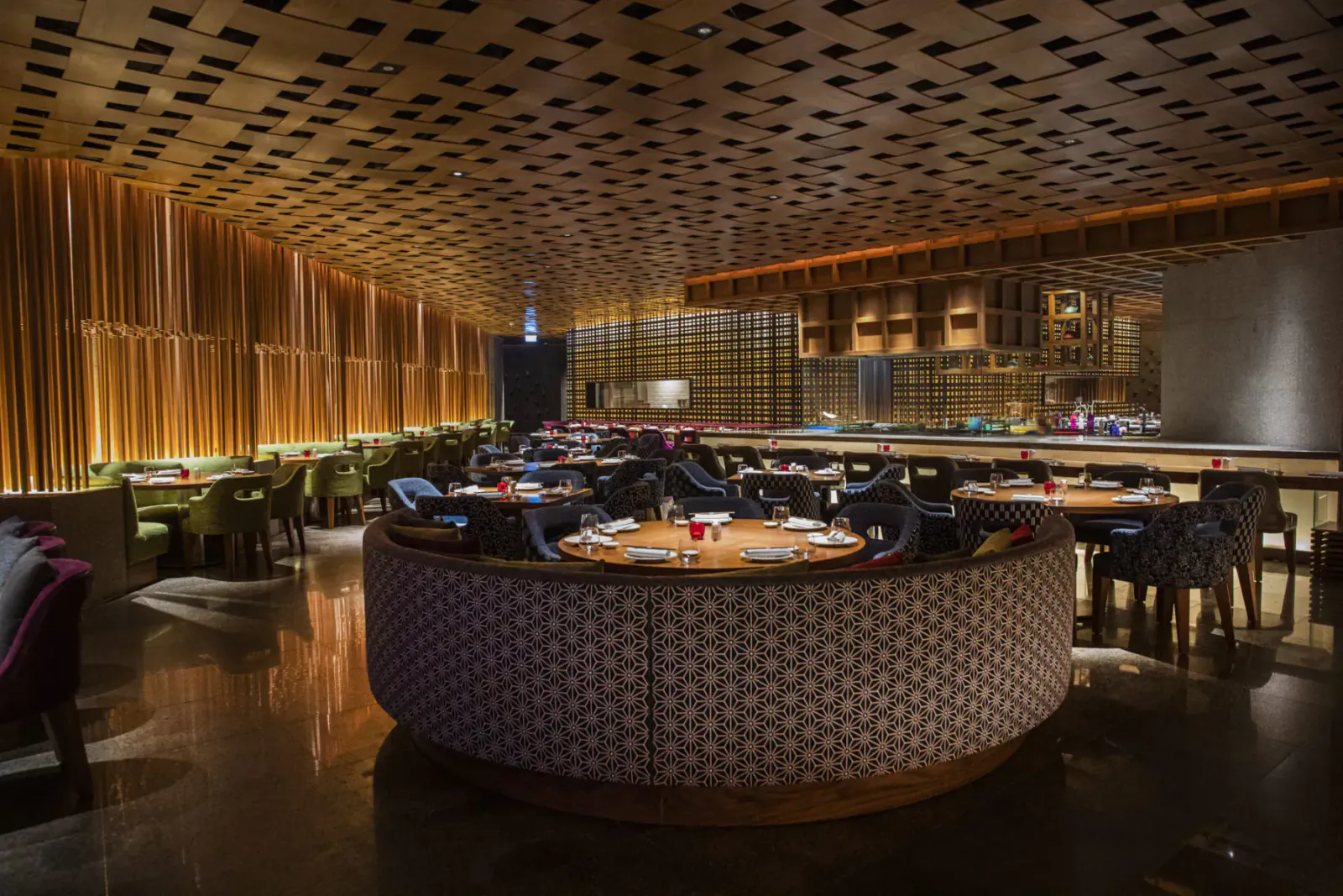 Elegant Myazú restaurant interior with wooden ceiling, curved bar, round tables, plush chairs, and warm lighting.