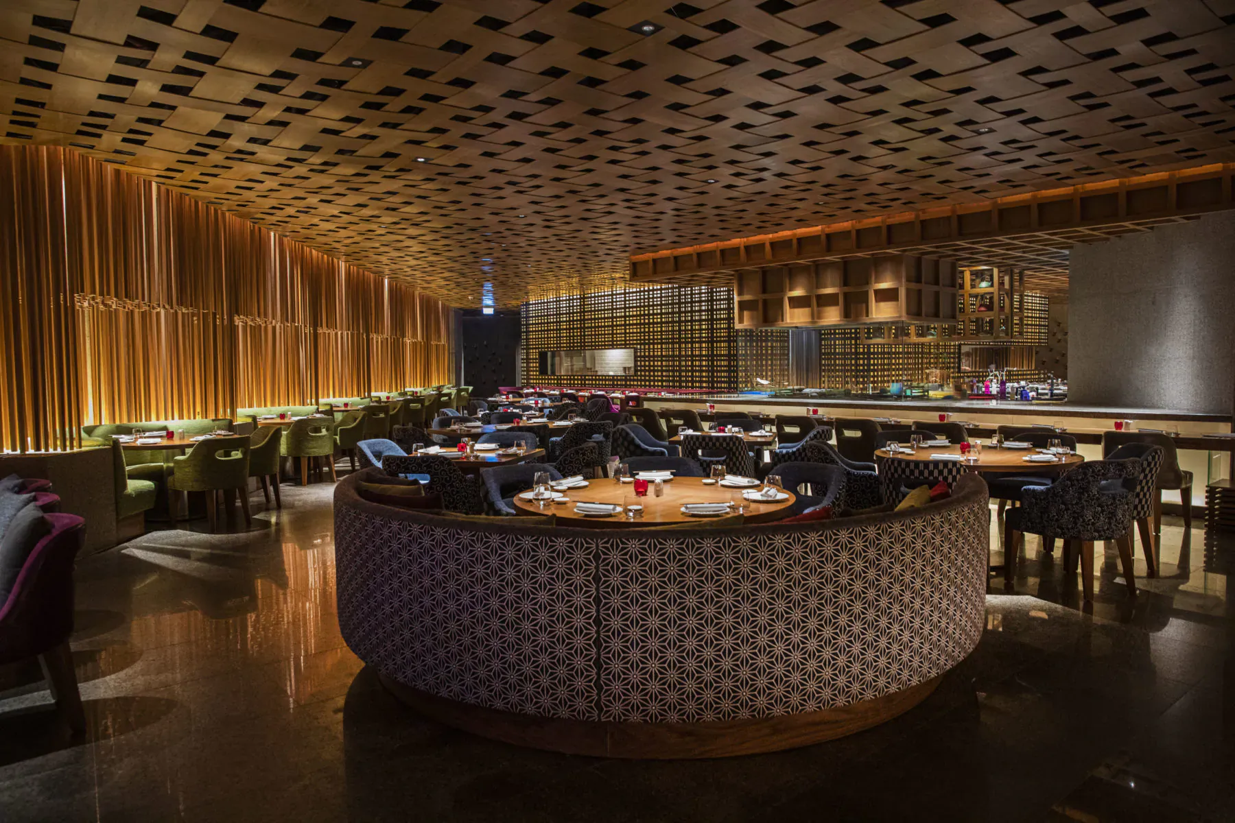 Elegant Myazú restaurant interior with wooden ceiling, curved bar, round tables, plush chairs, and warm lighting.
