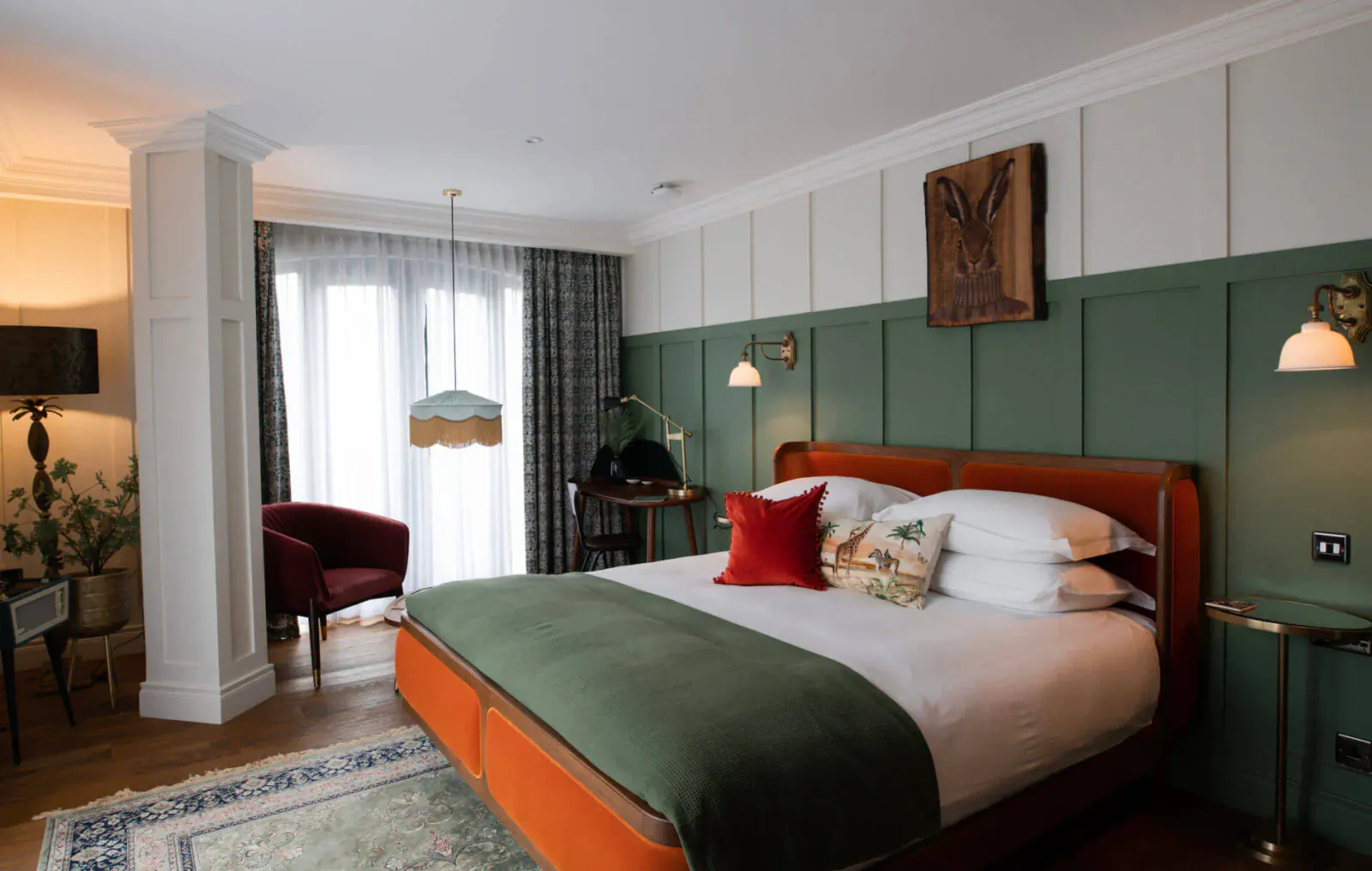 Stylish hotel bedroom at The Rabbit Hotel with green accent wall, wooden rabbit art, king bed with green bedding, and plush armchair.