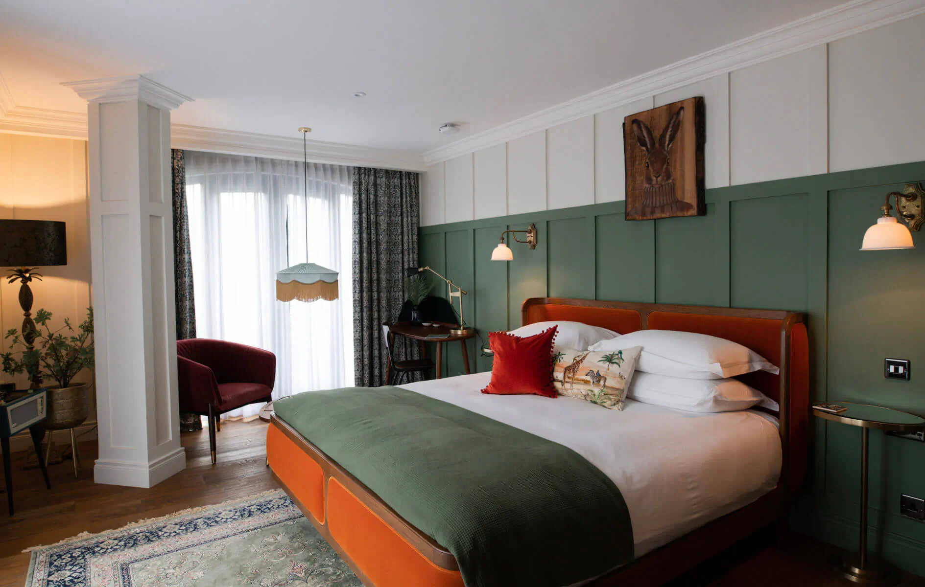 Stylish hotel bedroom at The Rabbit Hotel with green accent wall, wooden rabbit art, king bed with green bedding, and plush armchair.