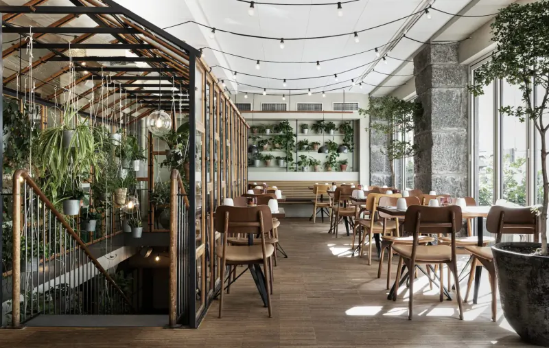 Hotel SP34 Gallery in Copenhagen: greenhouse-style dining area with wooden chairs, lush plants, string lights, stone walls.