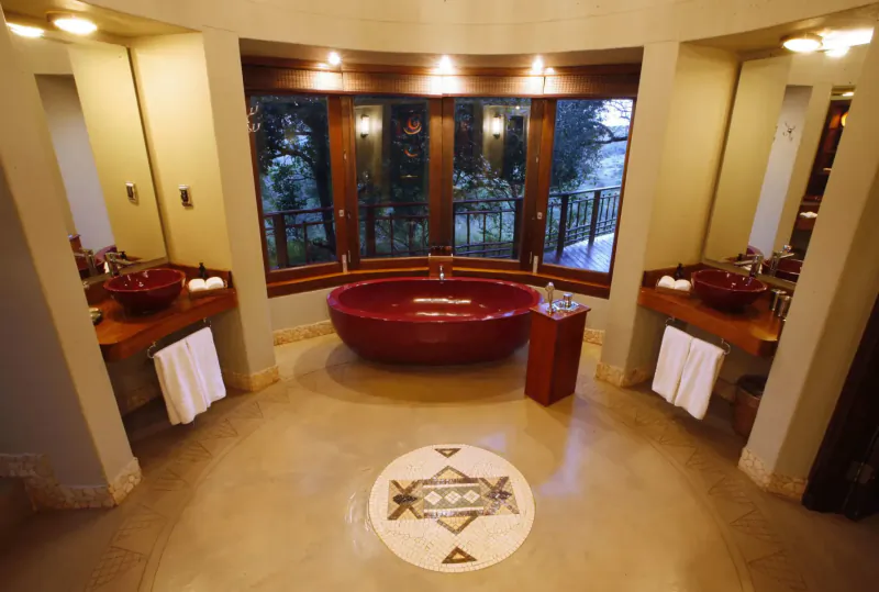 Luxurious circular bathroom at Thanda Safari with red bathtub, wooden vanities, jungle view, and geometric floor design.