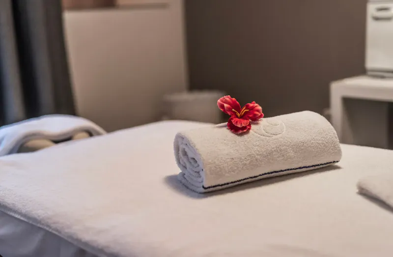 Rolled white towel with red hibiscus flower on massage table in spa room