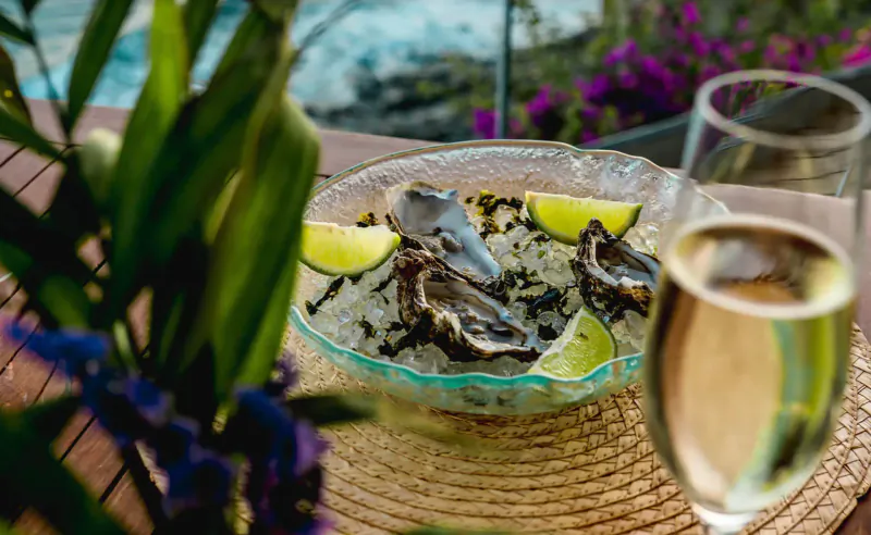 Oysters with lime in glass bowl on seaside wooden deck with champagne glasses and tropical plants