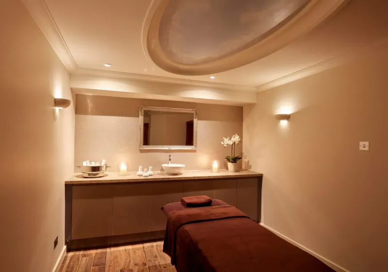 Elegant spa treatment room with massage table, sink, orchids, and warm lighting