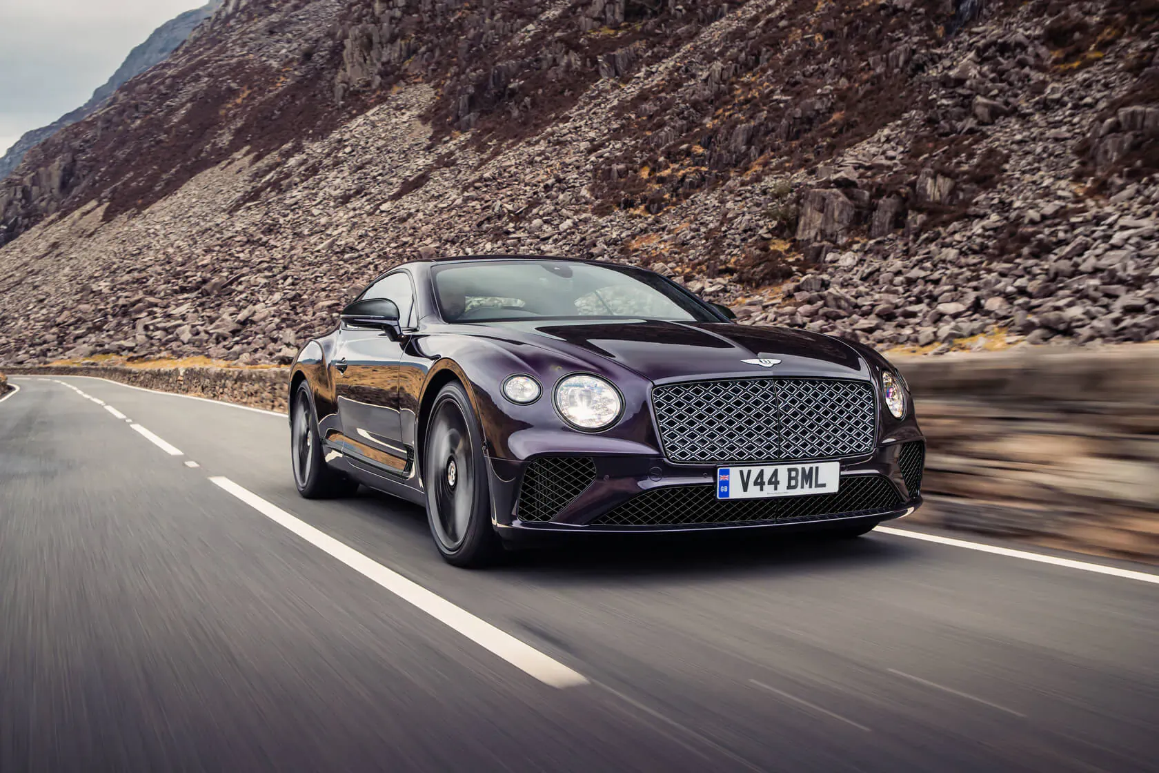 Purple Bentley GT Mulliner Blackline speeding on mountain road, license plate V4 GTML