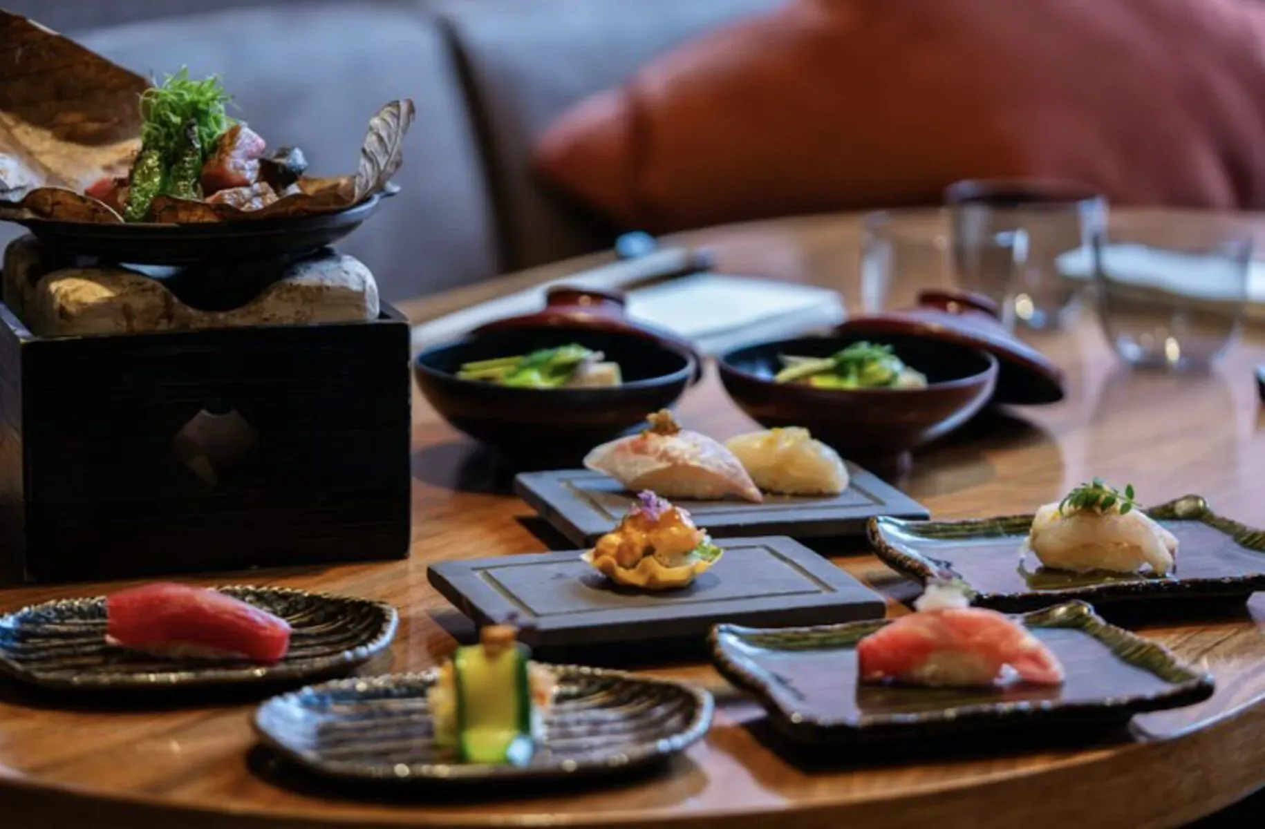 Assortment of sushi and sashimi on plates and bowls on a wooden table in elegant setting