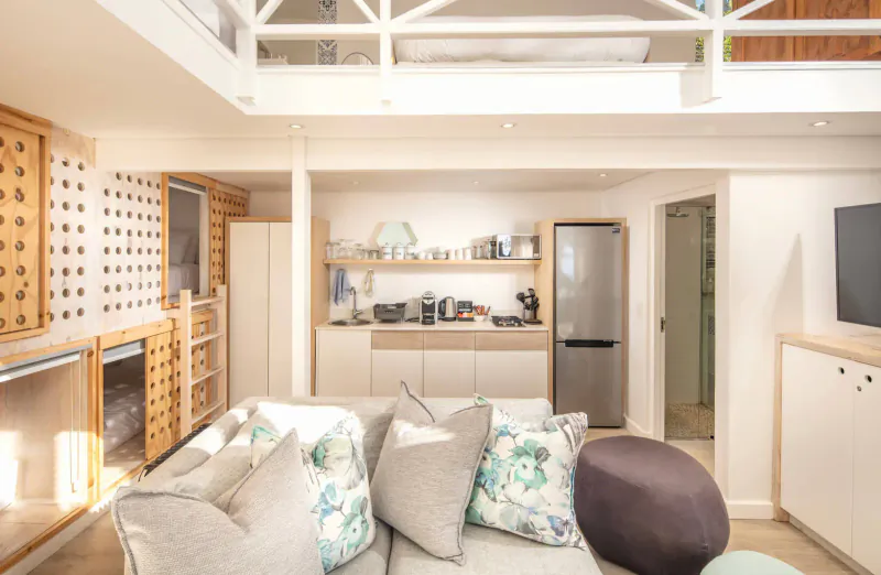 Cozy seaside bungalow living room with loft mezzanine, floral sofa, kitchenette, and TV.