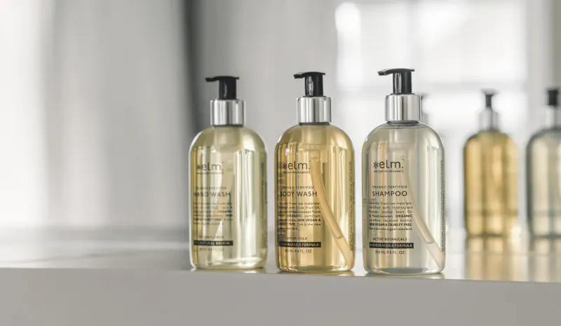 Row of Elm Organics shampoo and conditioner bottles in clear glass with pump tops on a table