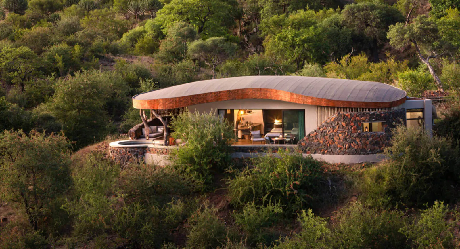 Mashatu Euphorbia eco camp: curved copper-roofed luxury cabin with hot tub on lush green hillside.