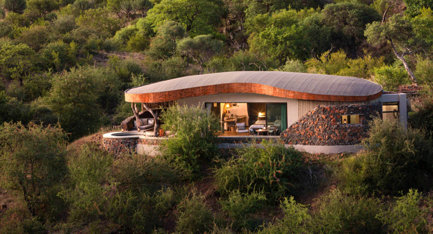 Mashatu Euphorbia eco camp: curved copper-roofed luxury cabin with hot tub on lush green hillside.