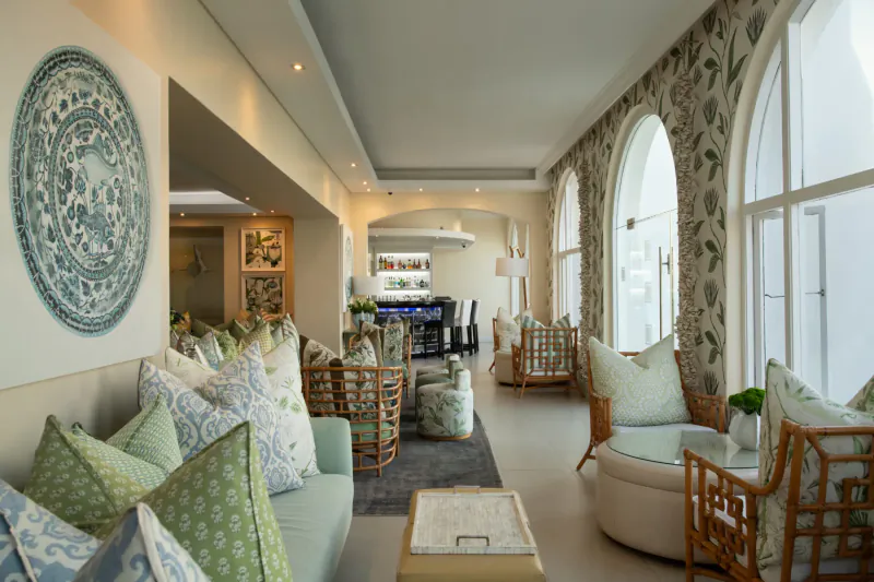 Elegant hotel lounge at The Marine Hotel Hermanus with plush green and white cushions, wicker chairs, blue bar, and arched windows.