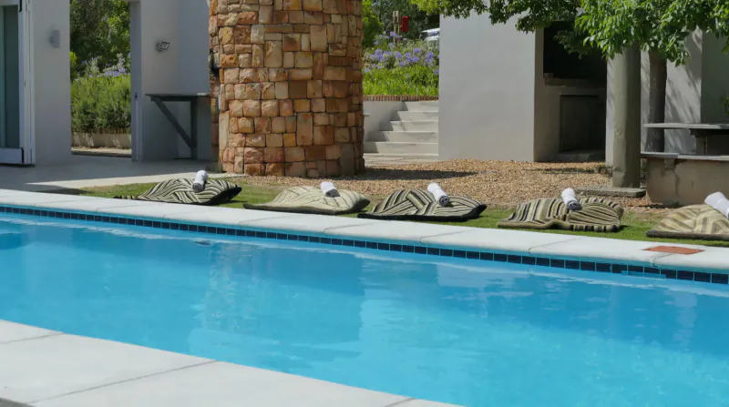 Blue swimming pool at South Hill Vineyards in Elgin Valley, with lounge chairs, stone pillars, and vineyards.