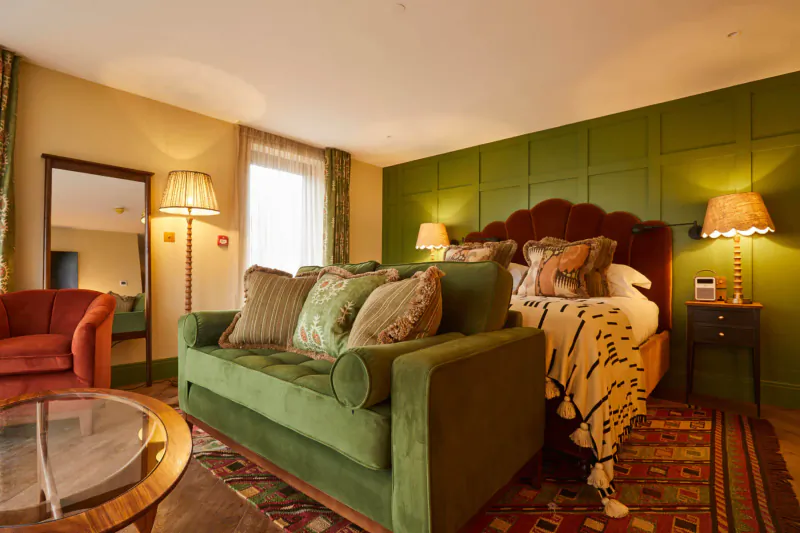 Elegant Rothay Manor hotel bedroom with green velvet sofa, ornate bed, lamps, and patterned rug.