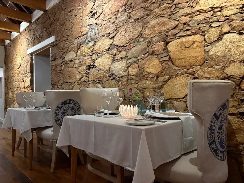 Elegant dining table set in rustic stone-walled room at The Old Rectory, with white linens, blue chairs, wine glasses, and candle.