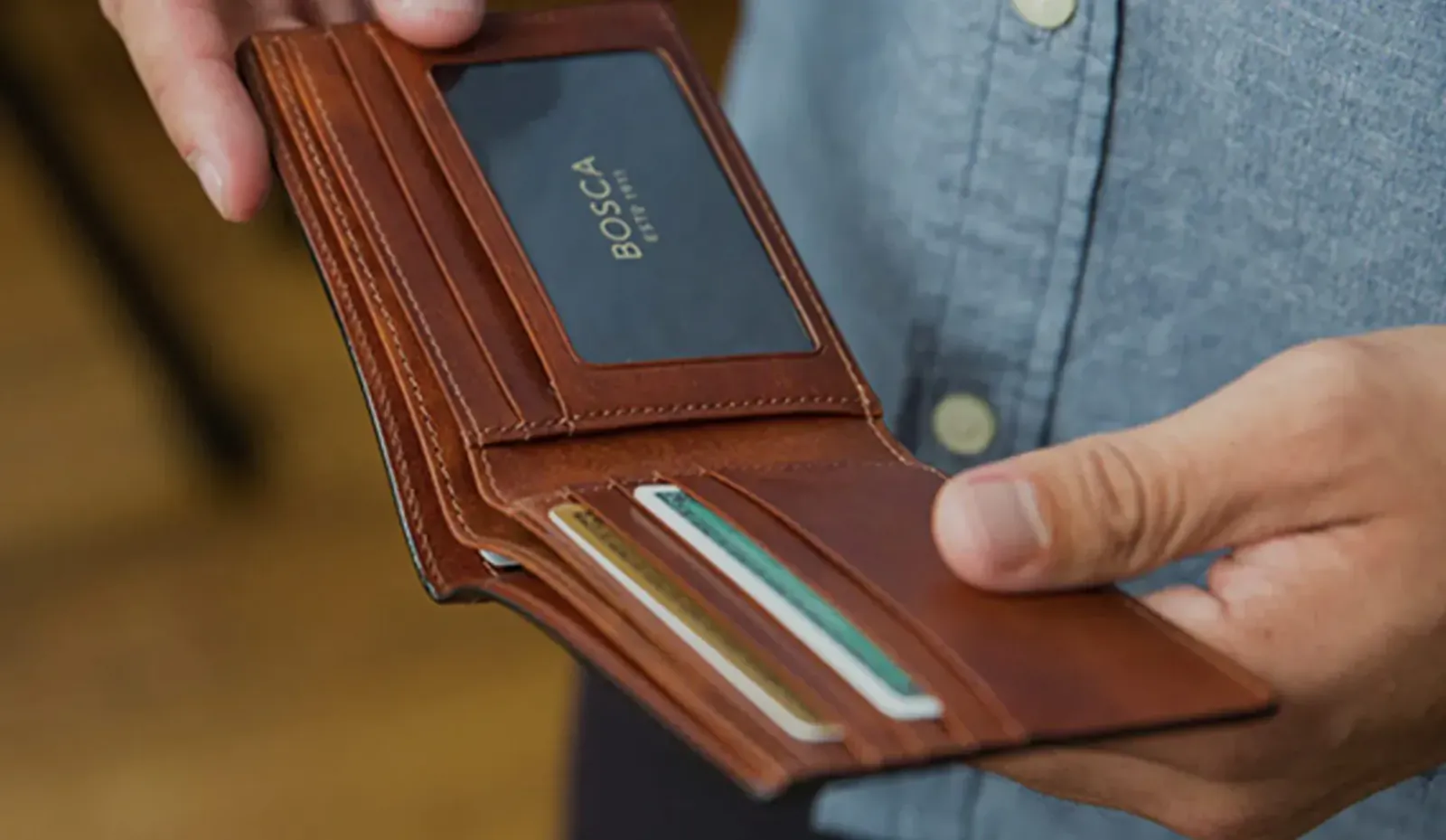 Man's hand holding open tan leather Borsa wallet displaying cards inside
