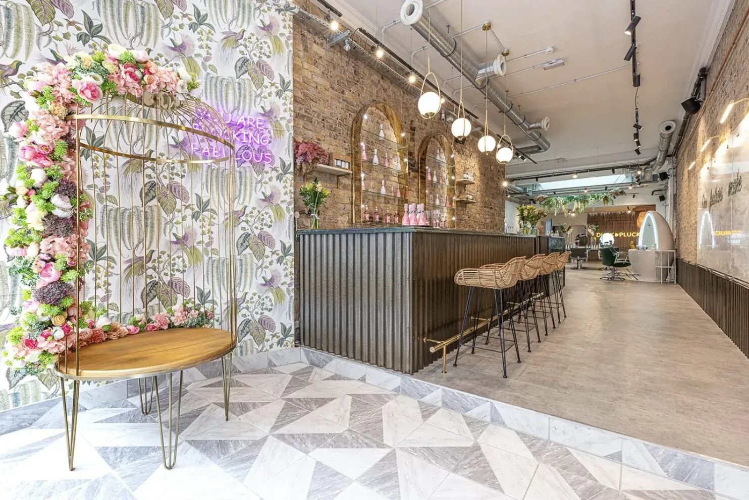 Duck & Dry salon interior: floral arch, purple orchids, wooden bar with rattan stools, exposed brick and pendant lights.