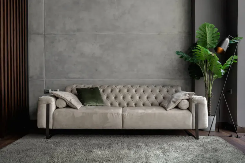 Beige tufted sofa with green pillows in modern gray room with plants and wood panels