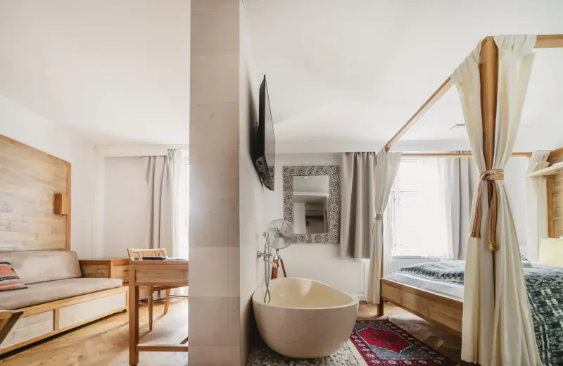 Elegant hotel suite with wooden four-poster bed, freestanding bathtub, desk, and TV at Manon Les Suites.